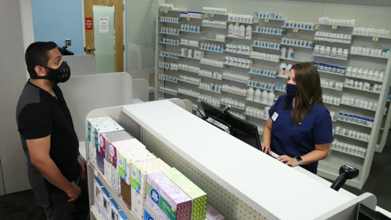 A customer and pharmacist engage in a conversation at a pharmacy counter