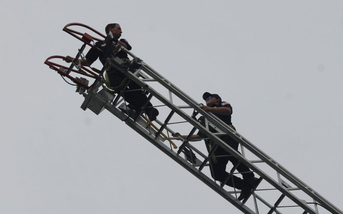 two firefighters talking while on a fire truck's ladder.