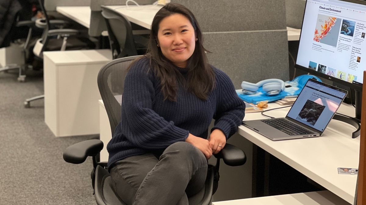 Delger Erdenesanaa poses for a photo while sitting a desk in a newsroom.