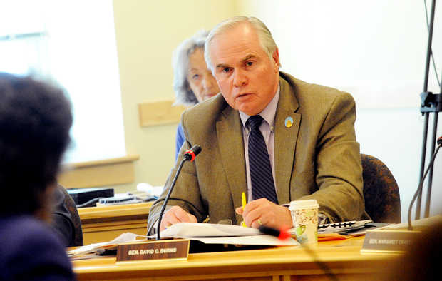 David C. Burns speaks into a microphone while sitting at his desk in the maine state house
