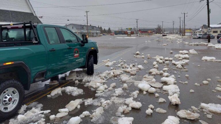 water and clumps of snow cover the roadway.