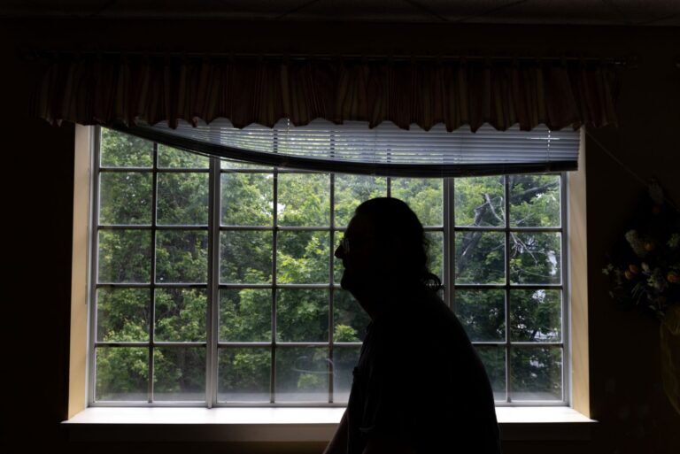 a silhouetted man stands in front of a window.