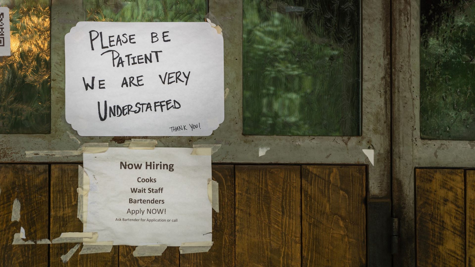 two help wanted signs seen on a restaurant wall
