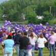 A large group of people prepare to release the purple balloons they are holding