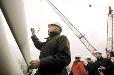 Paul Gaynor wearing a hard hat signs his signature to a blade of a windmill at a construction project