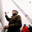 Paul Gaynor, wearing a hard hat, signs his signature onto the blade of a windmill