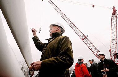 Paul Gaynor, wearing a hard hat, signs his signature onto the blade of a windmill