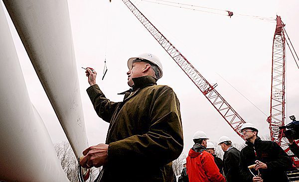 Paul Gaynor, wearing a hard hat, signs his signature onto the blade of a windmill