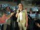 Cynthia Dill speaks into a microphone at a campaign event with a group of supporting, many holding blue signs with DILL on them standing behind her