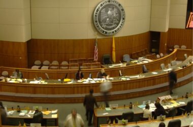 Overhead view of the inside of the New Mexico state legislature room filled with state lawmakers sitting at their desks and walking around.