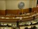 Overhead view of the inside of the New Mexico state legislature room filled with state lawmakers sitting at their desks and walking around.