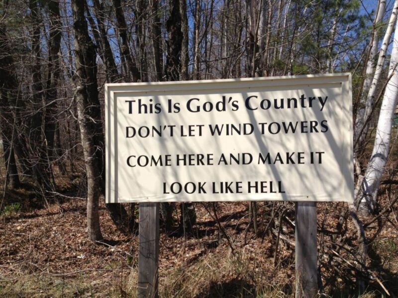 a sign in the woods that reads this is God's country don't let wind towers come here and make it look like hell