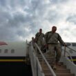 Soldiers walk down a flight of stairs that was pushed up against the commercial airplane they were riding in