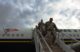 Soldiers walk down a flight of stairs that was pushed up against the commercial airplane they were riding in