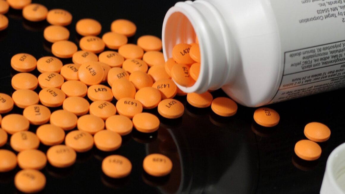 Many orange aspirin pills scattered on a table after being dumped from a bottle.