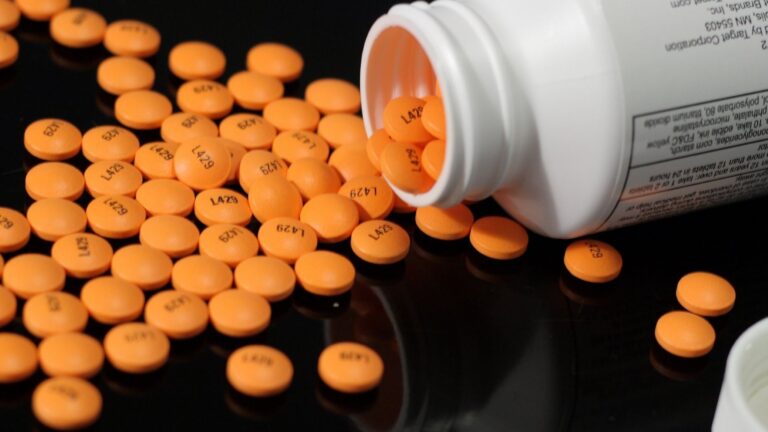 Many orange aspirin pills scattered on a table after being dumped from a bottle.