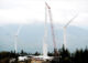 A crane operator lowers the top tower section while building wind turbines