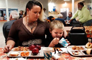 a mother wraps her arm around her son while he eats