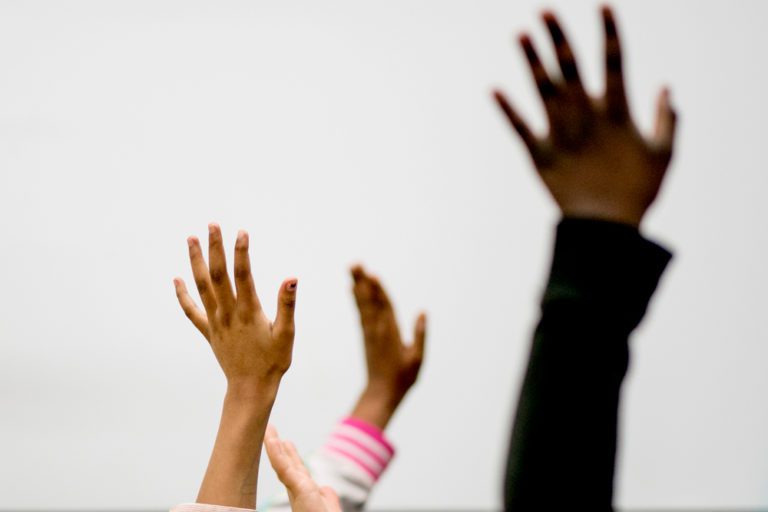 Three students' hands are raised in the air.