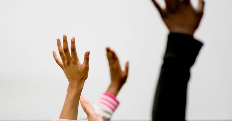 Three students' hands are raised in the air.