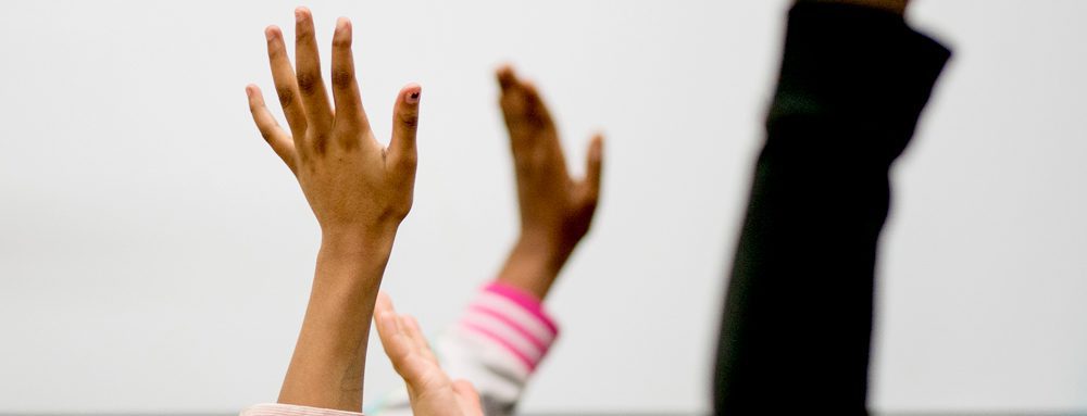 Three students' hands are raised in the air.