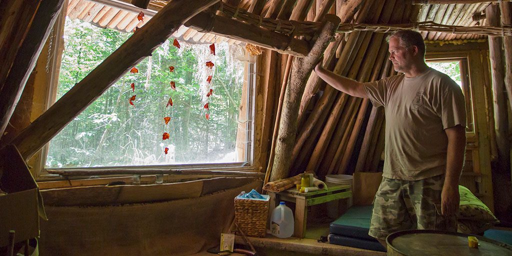 Michael Douglas, owner of Primitive Skills School, looks out the window of one of four experimental shelters at the school. Photo by Jill Brady.