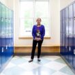Janis Hogan stands in a hallway at Camden Hills Regional High School surrounded by blue lockers.