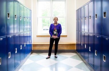 Janis Hogan stands in a hallway at Camden Hills Regional High School surrounded by blue lockers.