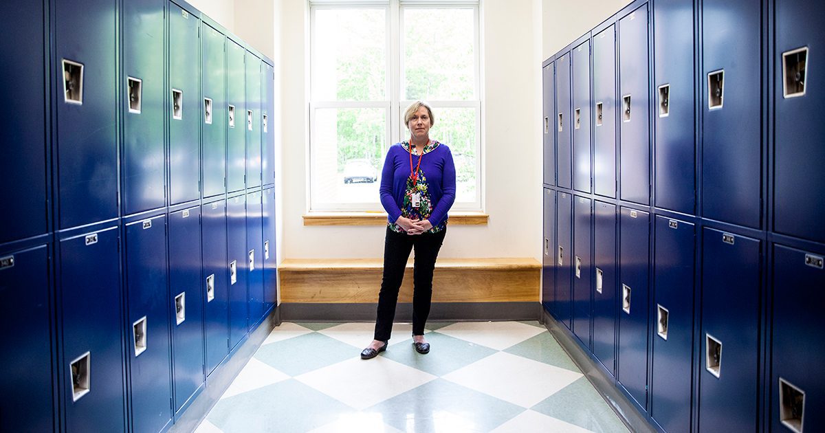 Janis Hogan stands in a hallway at Camden Hills Regional High School surrounded by blue lockers.