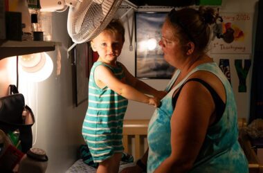 young boy stands on a table while gripping his mother's shirt