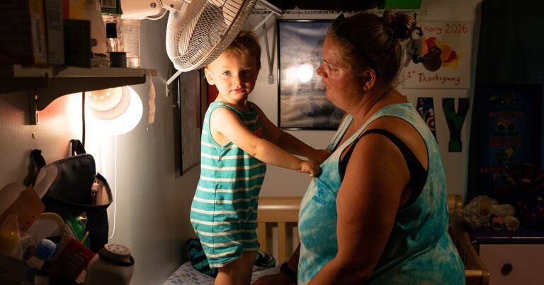 young boy stands on a table while gripping his mother's shirt