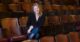 Amanda Huotari smiles and poses for a photo while sitting in a theater chair, surrounded by several rows of empty theater chairs.