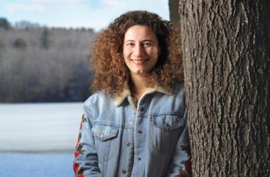 Rep. Chloe Maxmin smiles while posing for a photo and leaning against a tree.