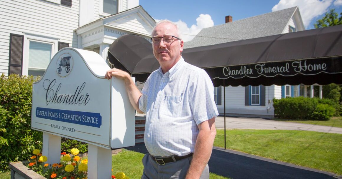 Dana Chandler poses for a photo alongside the sign in front of his business.