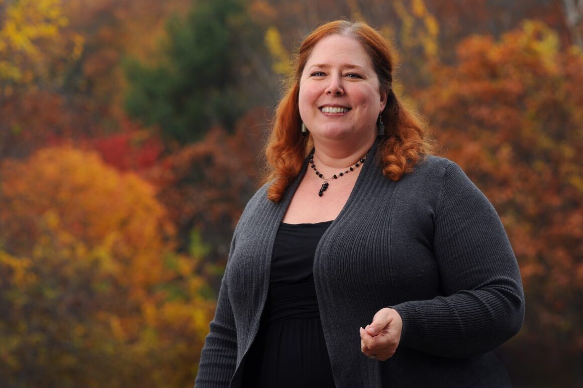Tiffany Bond poses for a photo with autumn trees in the background.