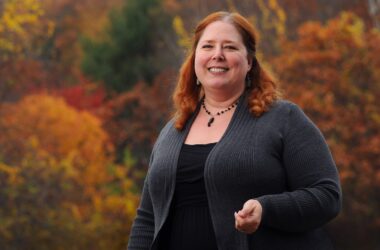 Tiffany Bond poses for a photo with autumn trees in the background.