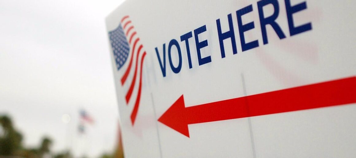 A white sign with a red arrow with "vote here" printed on the sign.