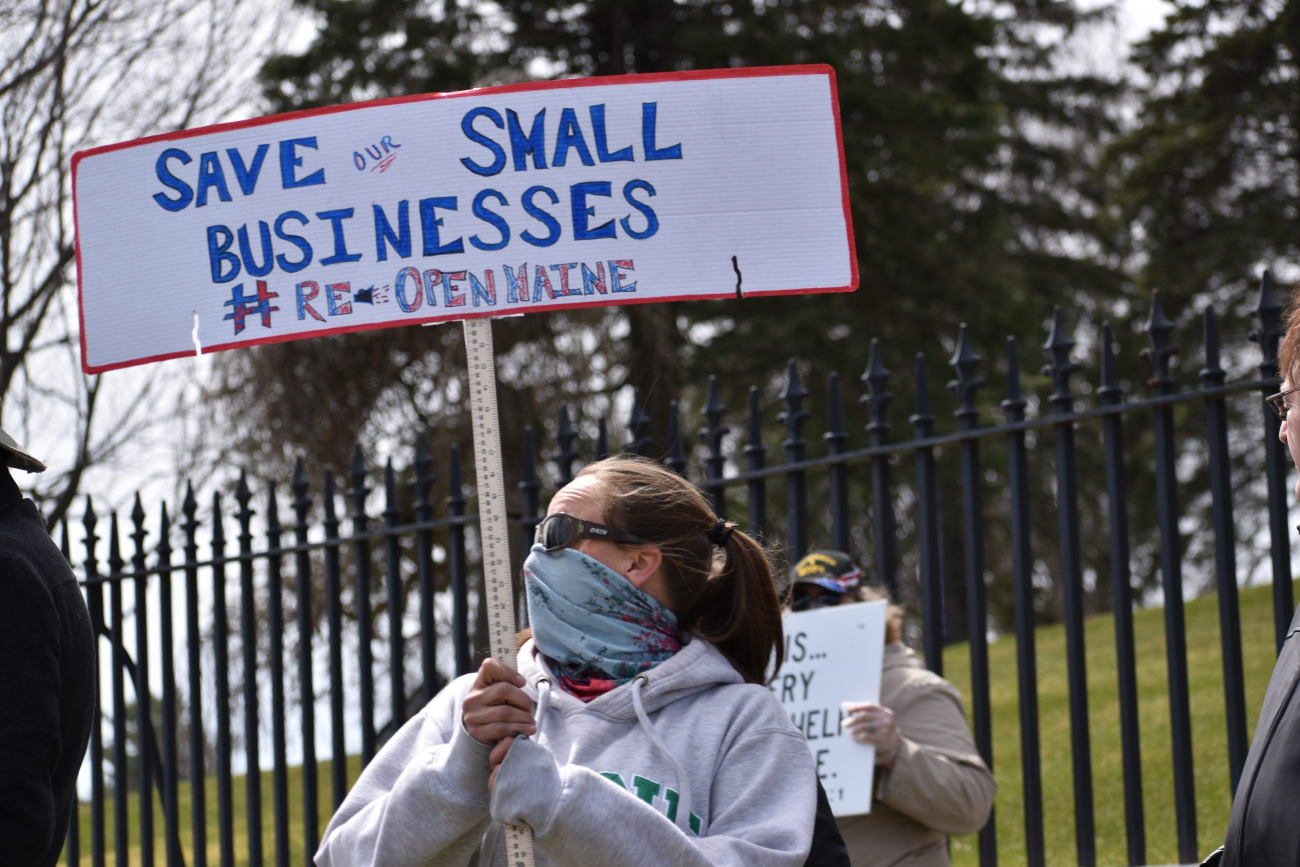 A protestor holds a sign that says save our small businesses re-open Maine