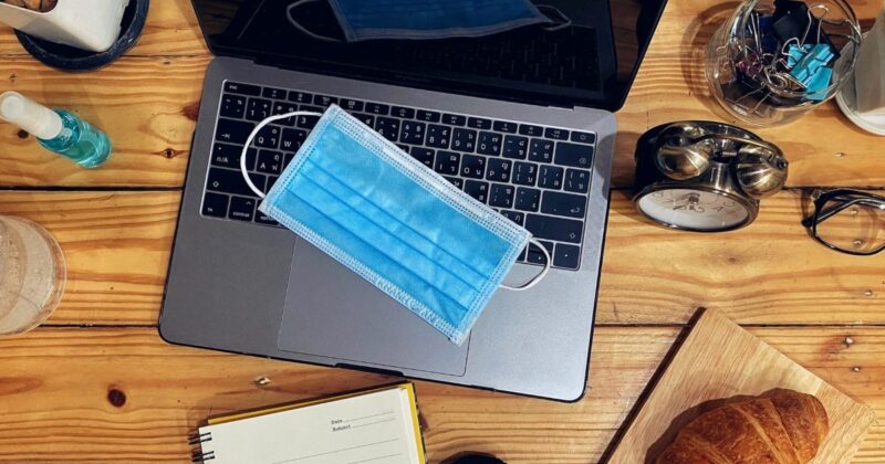 a blue covid mask sits on the keys of a laptop