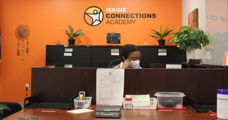 a woman talking on the phone at the reception desk for maine connections academy