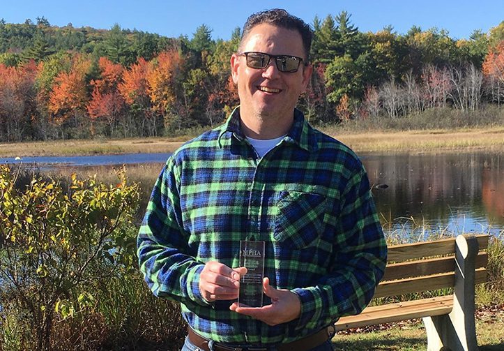 Dan Dinsmore holding a public health journalism award trophy from the Maine Public Health Association.