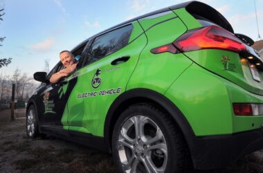 Dale Basher leans out the driver's window of a green electric vehicle belonging to Downeast Community Partners and poses for a photo.