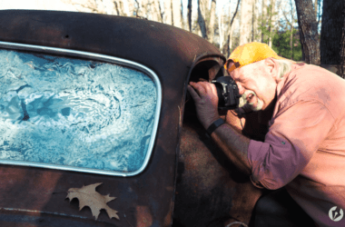 C. E. Morse leans ever so slightly into a junked car a junk yard with his camera to photograph the interior of the car.