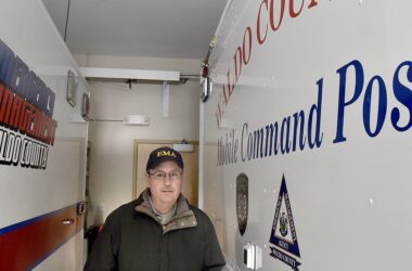 Emergency Management Director Dale Rowley stands within the agency's command center. To his left is a truck that reads "emergency management Waldo County" and to his right is a vehicle that reads "Waldo County Mobile Command Post."