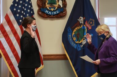 Sarah Churchill, on left, raises her right hand as she faces Governor Janet Mills, who is raising her right hand and reading from a piece of paper, during a swearing in ceremony in the governor's office.