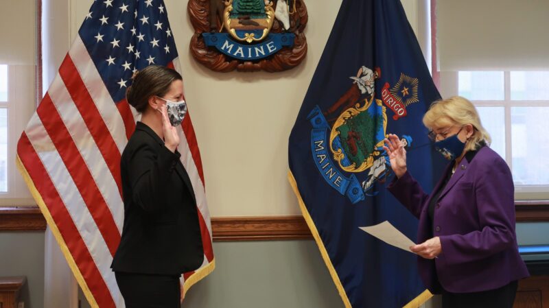 Sarah Churchill, on left, raises her right hand as she faces Governor Janet Mills, who is raising her right hand and reading from a piece of paper, during a swearing in ceremony in the governor's office.