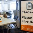 The entrance to a COVID-19 vaccination site in Bangor. Shown is the check-in table and a sign that reads "check-in please stop here. Northern Light Health COVID-19 vaccination site."