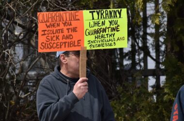 A man holds a sign during a protest outside the Maine State House. The reads: "Quarantine: When you isolate the sick and susceptible. Tyranny: When you quarantine health individuals and businesses."