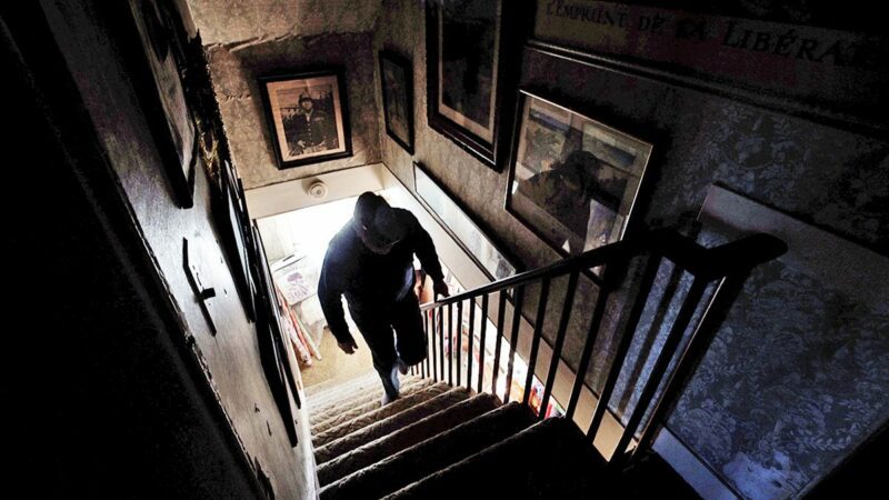 A man climbs up the stairs in an old farmhouse.