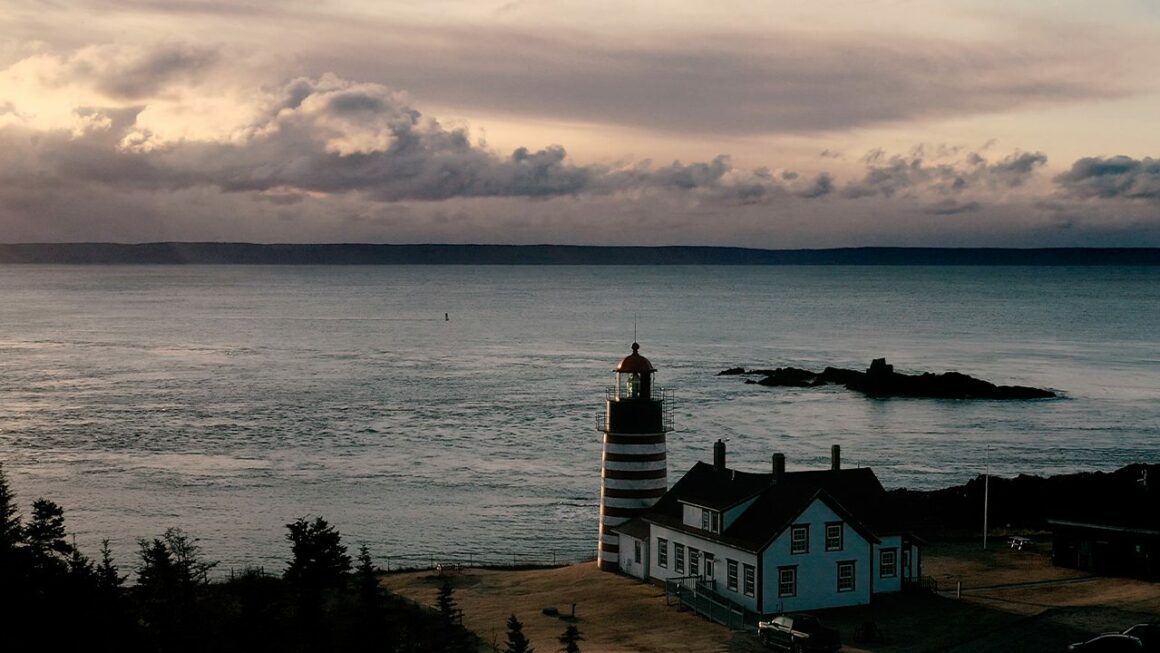 The West Quoddy Head Lighthouse, and the caretaker's house behind it, are shown at water's edge in Lubec, Maine.